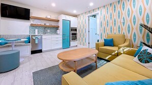 Un espacio habitable compacto con kitchenette, un sofá, una mesa de centro y una pared decorada.