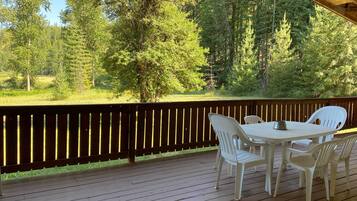 A wooden deck with a table and chairs, overlooking a forested area.