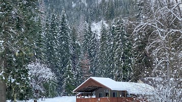 A cabin with a wooden deck, surrounded by snow-covered trees.