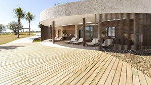 Un área de descanso moderna al aire libre con terraza de madera, sillones y un muro de piedra.