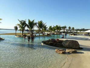 Un espace piscine avec une eau cristalline, des palmiers et un décor de plage.