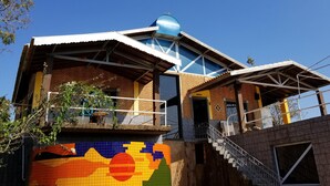 Un edificio de varios pisos con un mural de mosaico colorido en la pared inferior, una estructura en forma de cúpula azul en el techo y una escalera que conduce a un nivel superior.