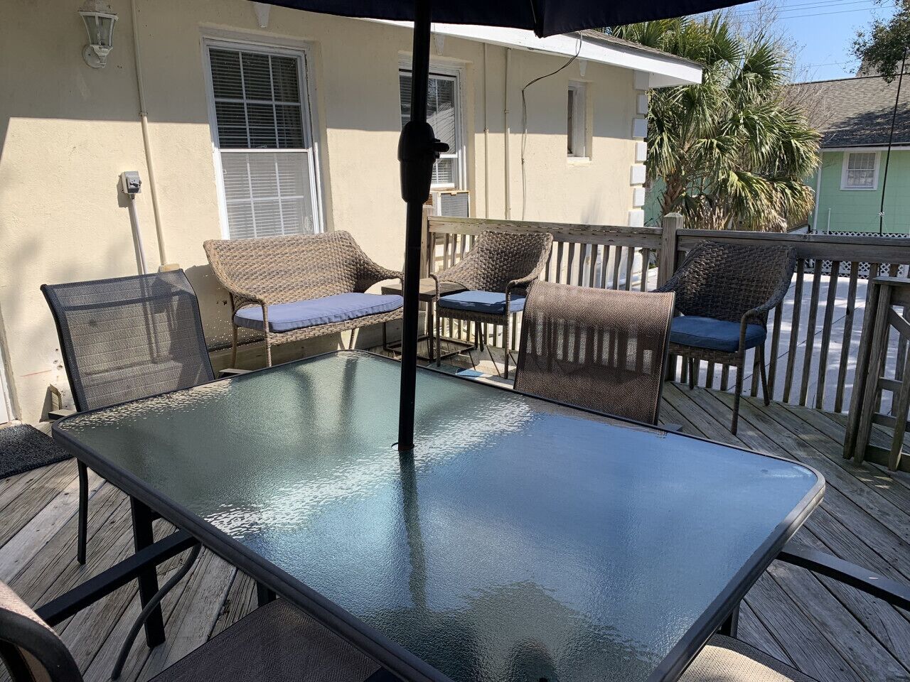 A glass-top table with metal legs, surrounded by wicker chairs with blue cushions.