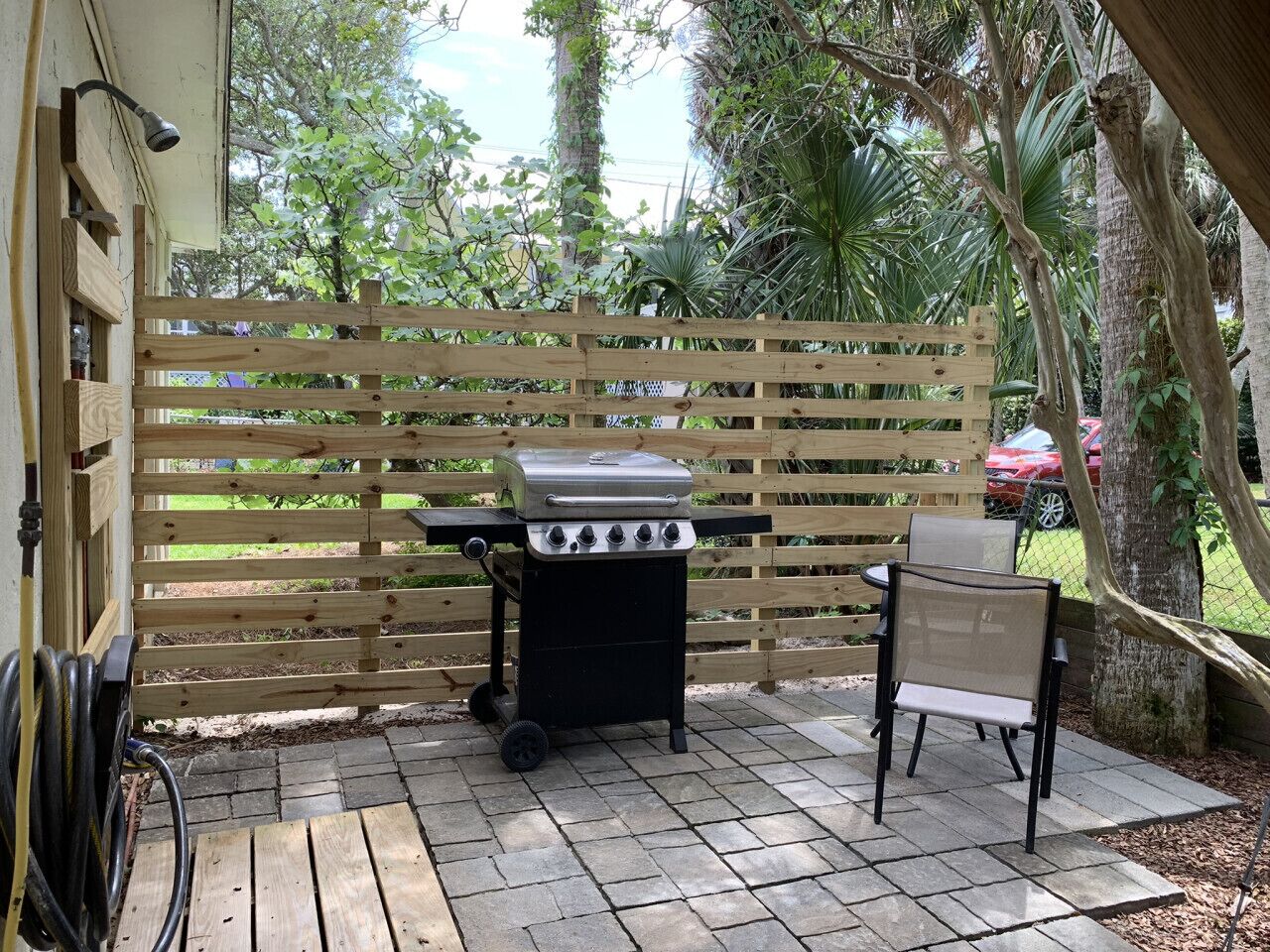 An outdoor patio with a grill, a chair, and a wooden fence.