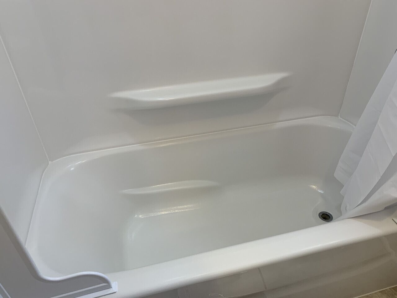 Et hvidt badekar med en hylde og afløb.