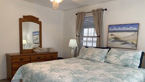 A bedroom with a bed, a dresser, a mirror, a window with curtains, and a painting on the wall. - ZenDeck & Courtyard - King Room & Double Room - Pet Friendly - Across from Beach (Charleston)