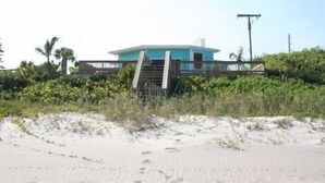 A single-story building with a flat roof, surrounded by dense vegetation and a sandy foreground. - Awesome direct ocean beach house! (cocoa beach)