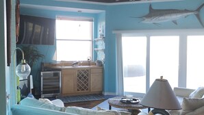 A room with a large fish mural on the ceiling, a TV mounted on the wall, a dining area with a table and chairs, and a window providing natural light. - Awesome direct ocean beach house! (cocoa beach)