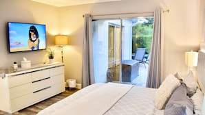 Een slaapkamer met een bed, een aan de muur bevestigde televisie, een nachtkastje met een lamp en een glazen schuifdeur naar een buitenruimte.
