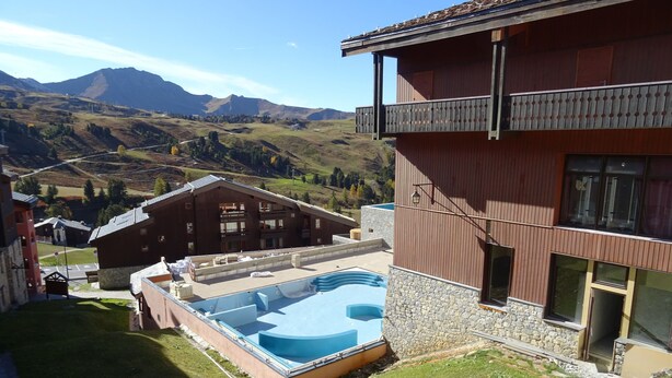 A building with a pool, stone walls, and a view of mountains. - Apartment 2 bedrooms 5/6 people duplex 38m2 at the foot of the slopes (La Plagne Tarentaise)