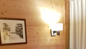 A wooden-paneled room with a brown sofa and patterned cushions, a framed picture, and a wall-mounted light fixture. - Apartment 2 bedrooms 5/6 people duplex 38m2 at the foot of the slopes (La Plagne Tarentaise)