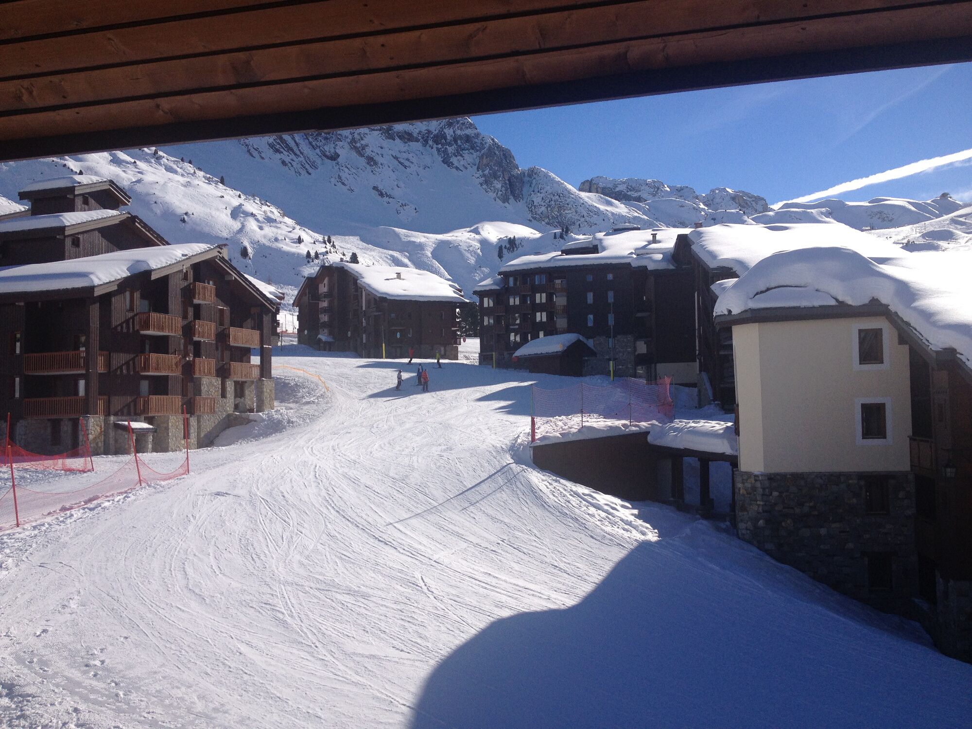 Un centro de esquí cubierto de nieve con edificios de madera, una pista de esquí y montañas al fondo.