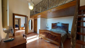 Un dormitorio con una cama de madera, un escritorio con un ventilador, un espejo y una escalera.