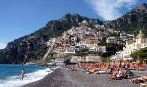Une plage bordée d’une côte rocheuse, une rangée de parasols et une colline parsemée de bâtiments.