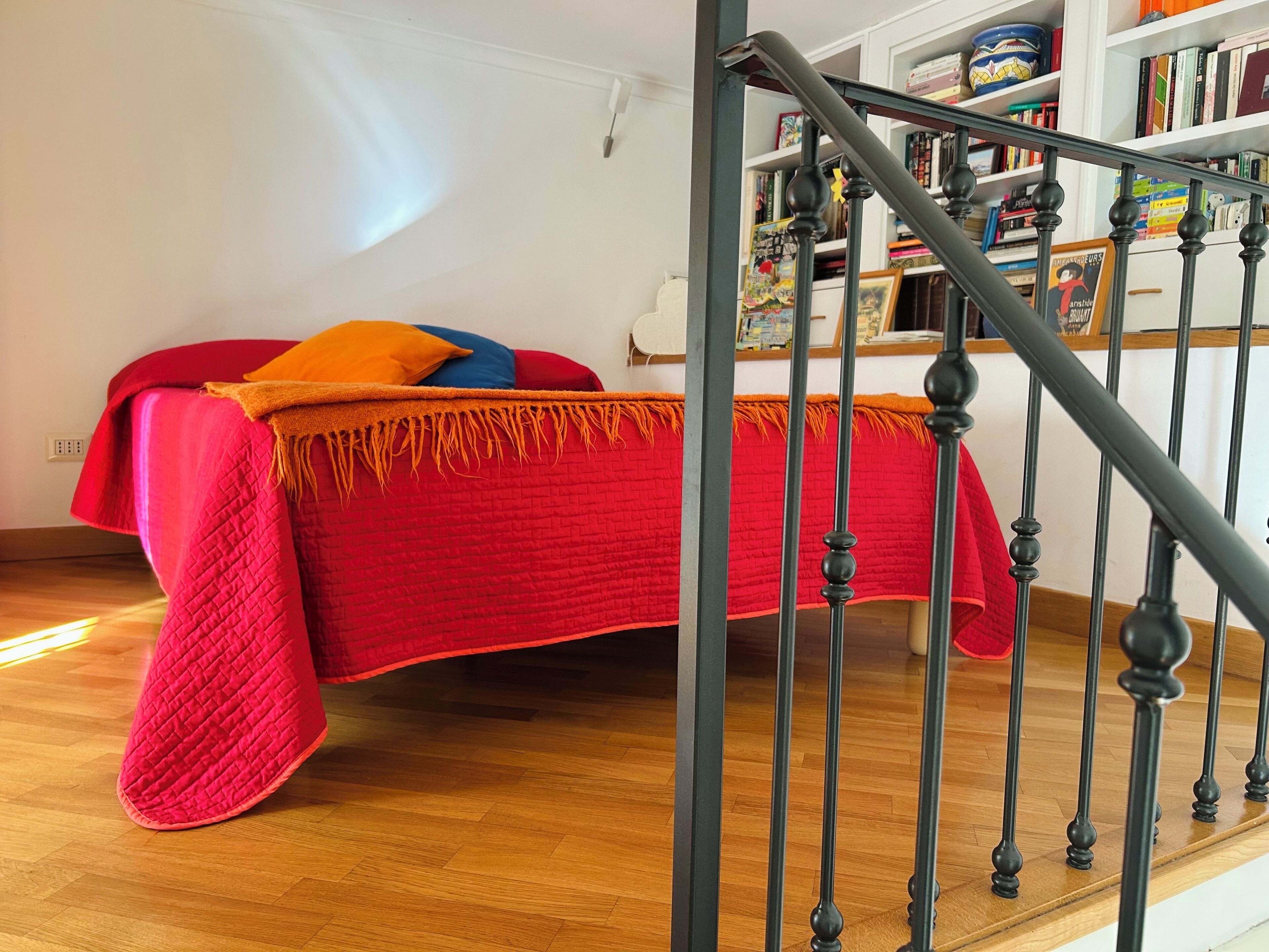 Une chambre à coucher avec un lit, une couverture rouge et un plancher en bois.