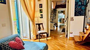 Quarto com cama, uma cadeira, janela com cortinas e vista para a cozinha.