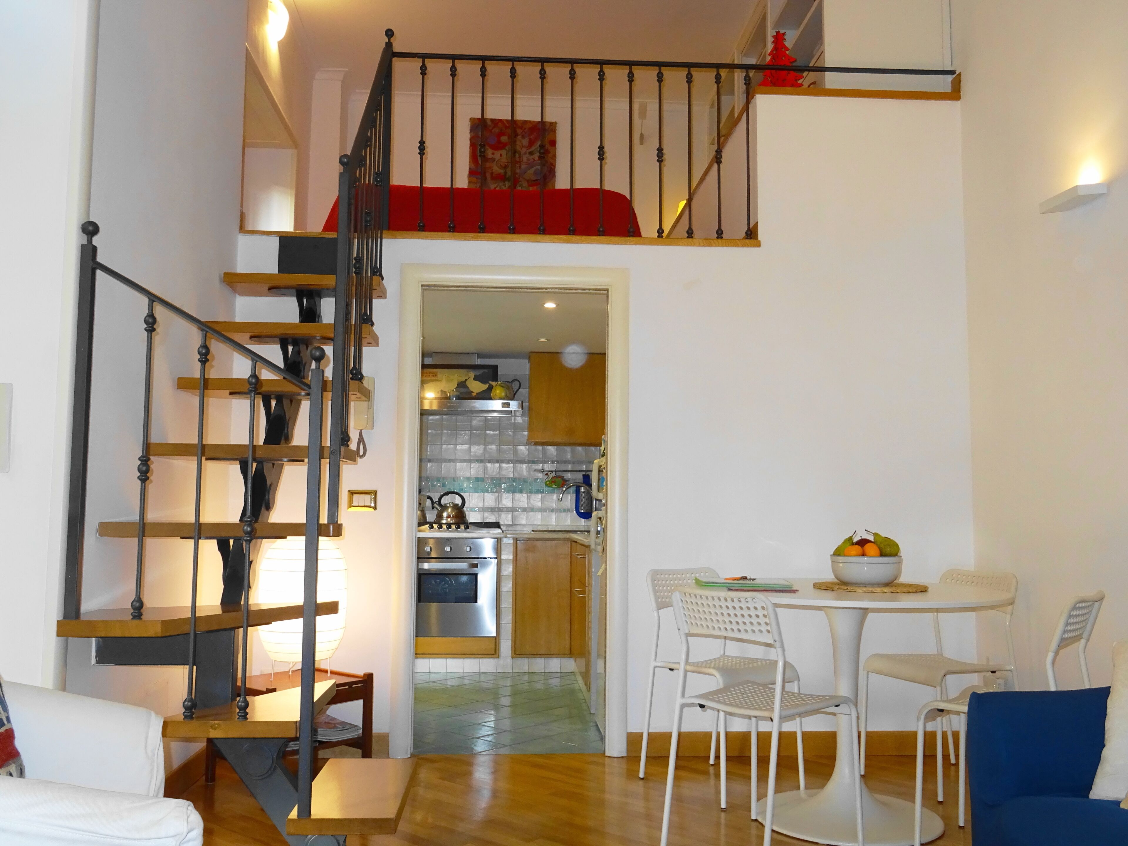 Ein kompakter Wohnraum mit Treppe zu einem Schlafzimmer auf dem Dachboden, einem Essbereich mit Tisch und Stühlen sowie einer Küchenzeile mit modernen Geräten.