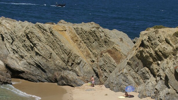 A beach with clear water, rocky cliffs, and a few people.
