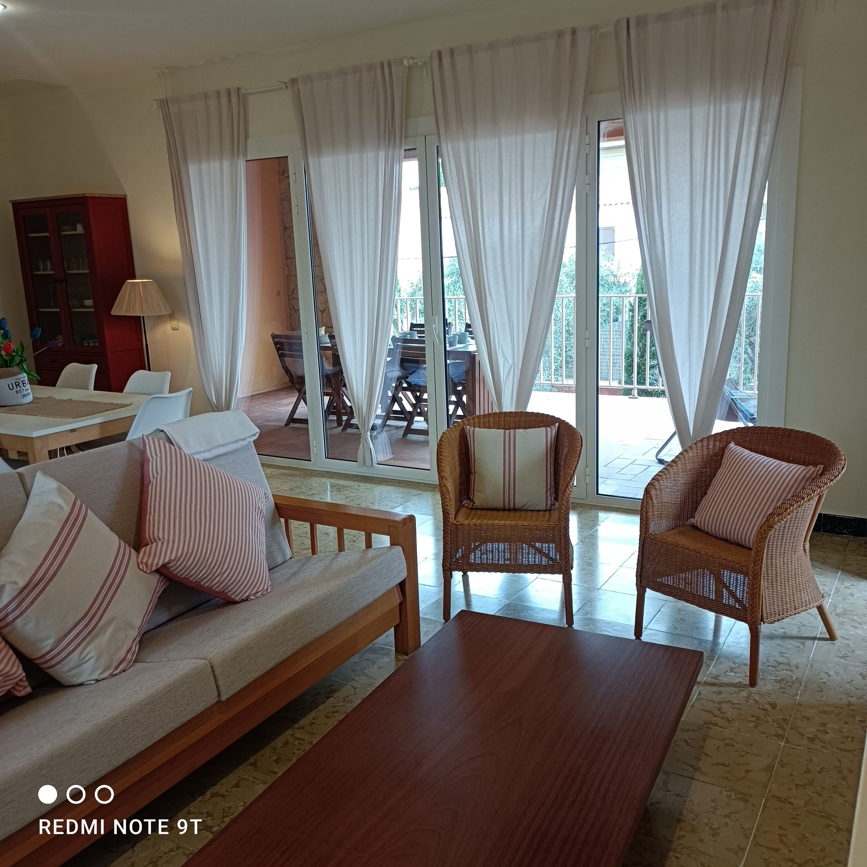 Un salon spacieux comprenant un canapé, deux fauteuils en osier, une table basse et un coin repas avec une table et des chaises.