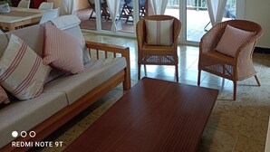 A spacious living room with a sofa, two wicker chairs, a coffee table, and a dining area with a table and chairs.