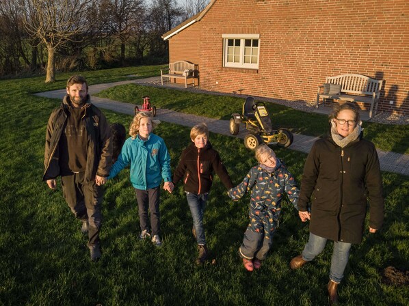 A group of people walking on a grassy path in front of a brick building with benches and a lawnmower.