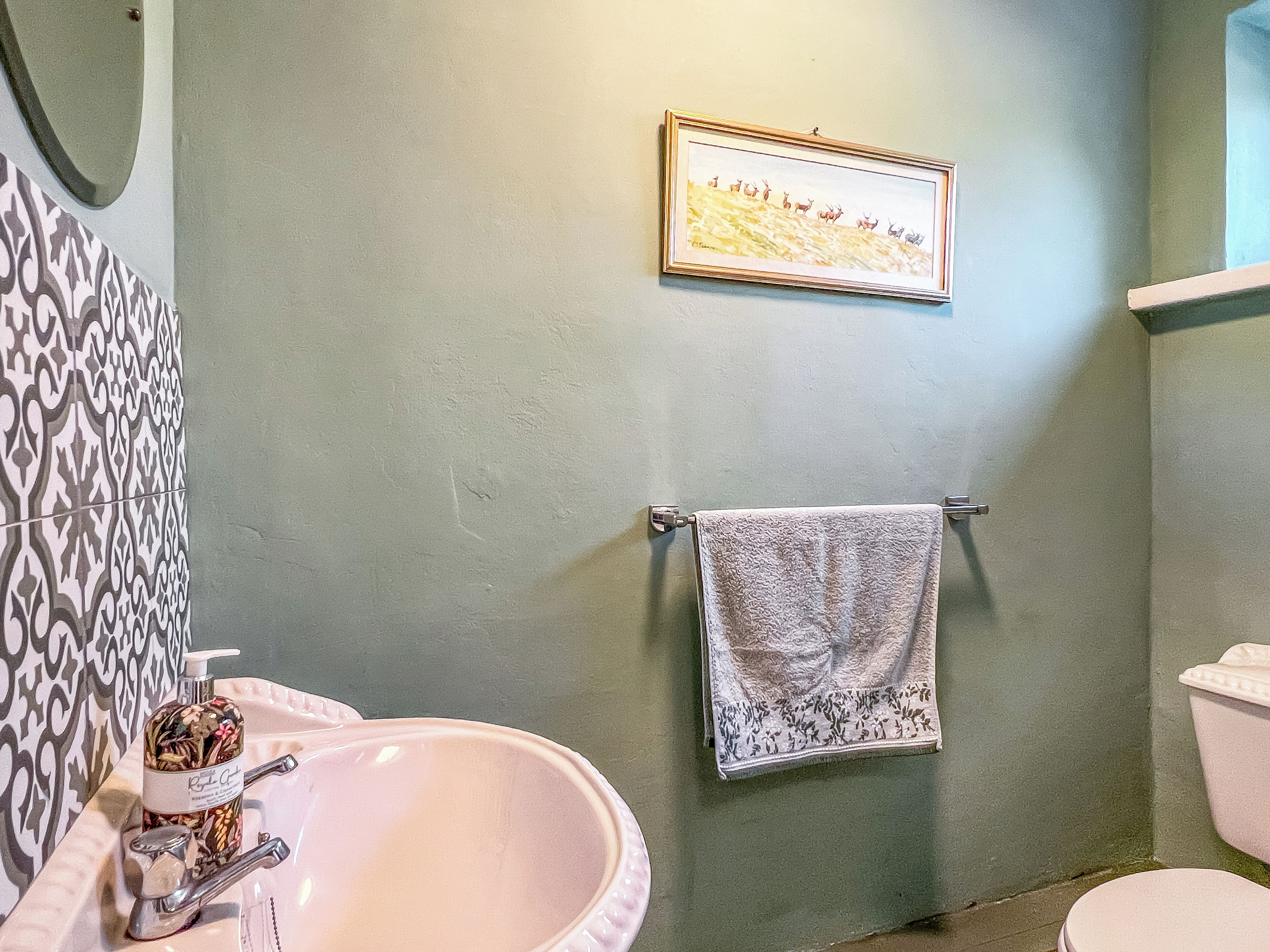 Une salle de bain avec un lavabo, des toilettes, un mur à motifs et un tableau encadré.