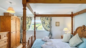 A four-poster bed with a wooden headboard, a wooden dresser, and a window with curtains. - Brook Cottage, Challacombe (Challacombe)