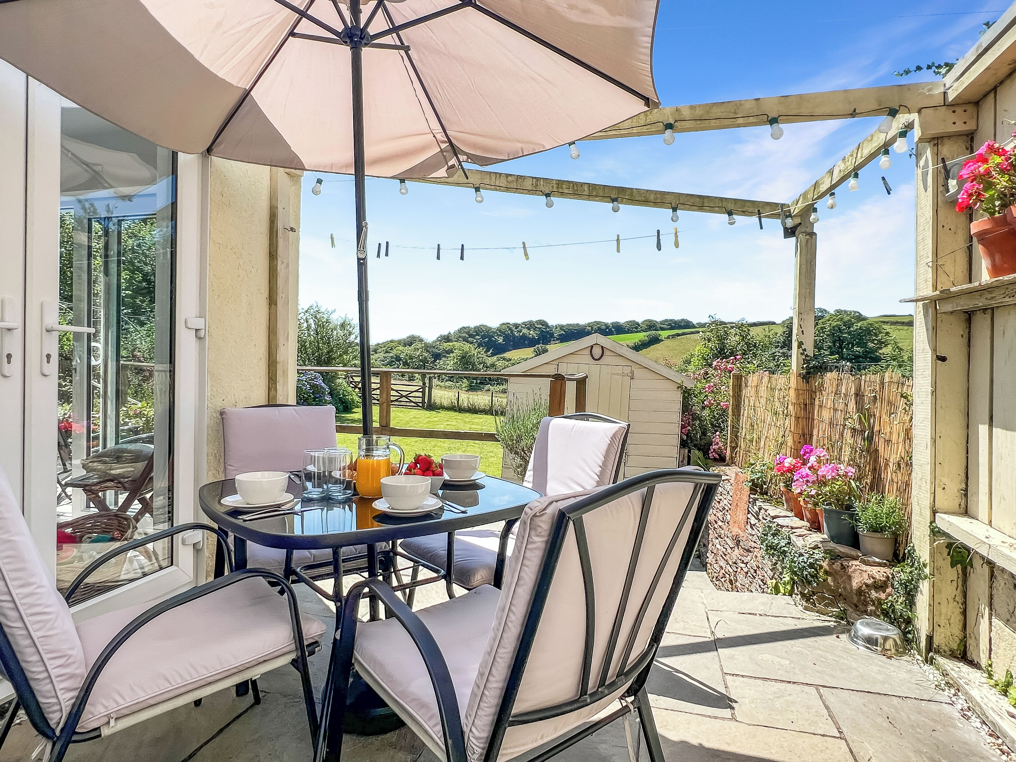 An outdoor patio with a table and chairs, a pergola with string lights, and a view of the countryside.