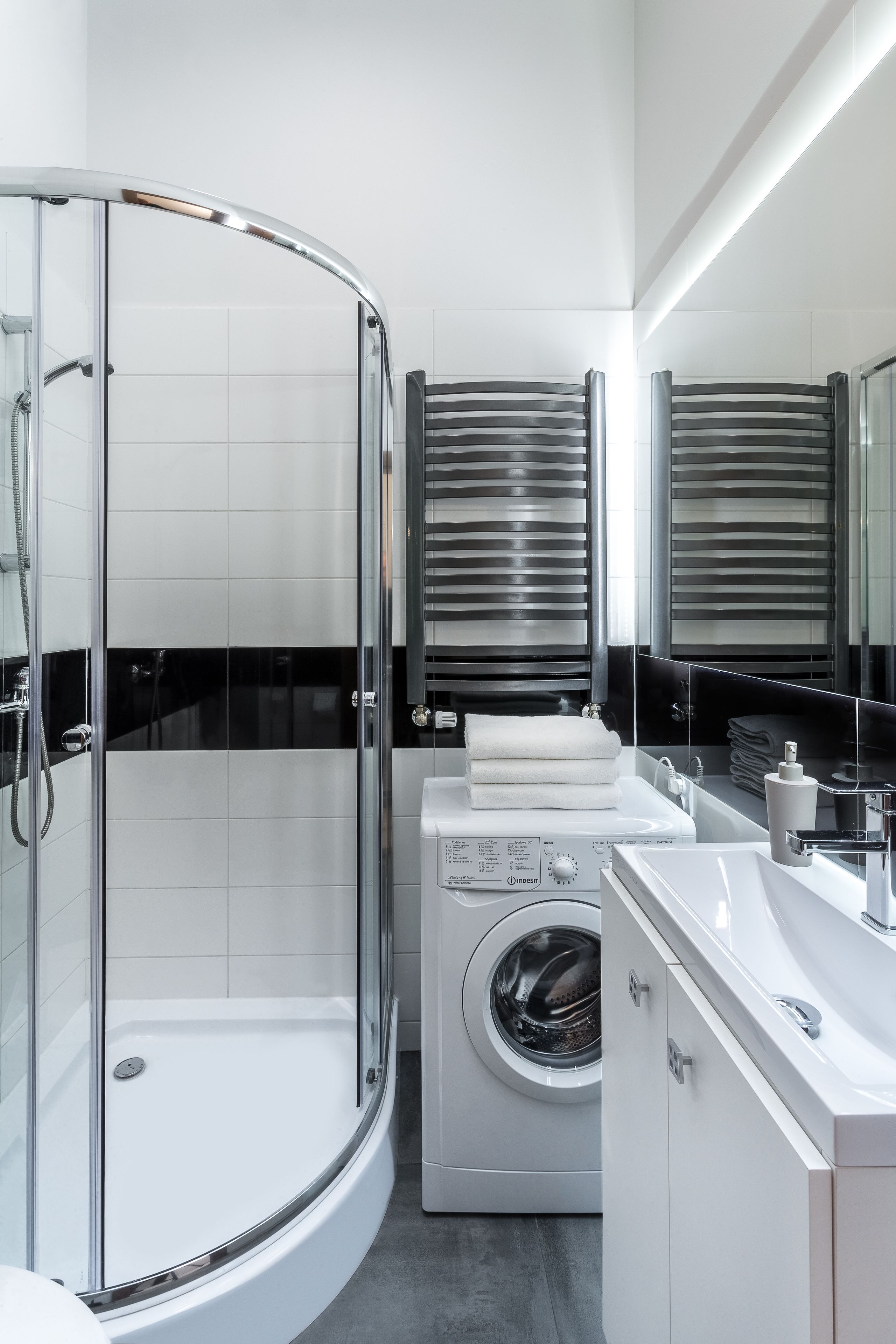 Un baño moderno con ducha envuelta en vidrio, lavadora integrada y un espejo grande.