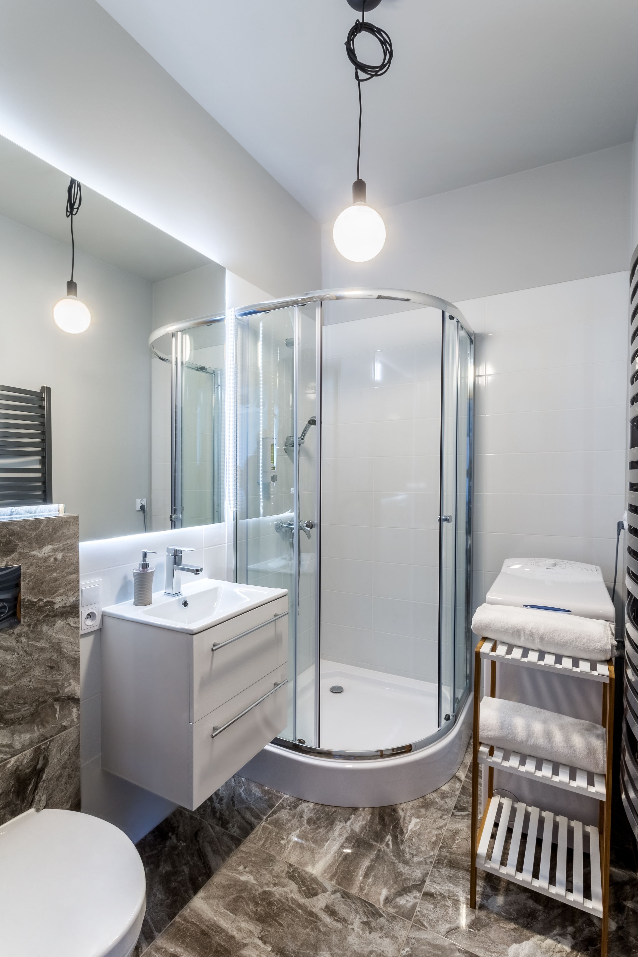 Een moderne badkamer met een douchecabine van glas, een wit wastafelmeubel en een marmeren vloer.