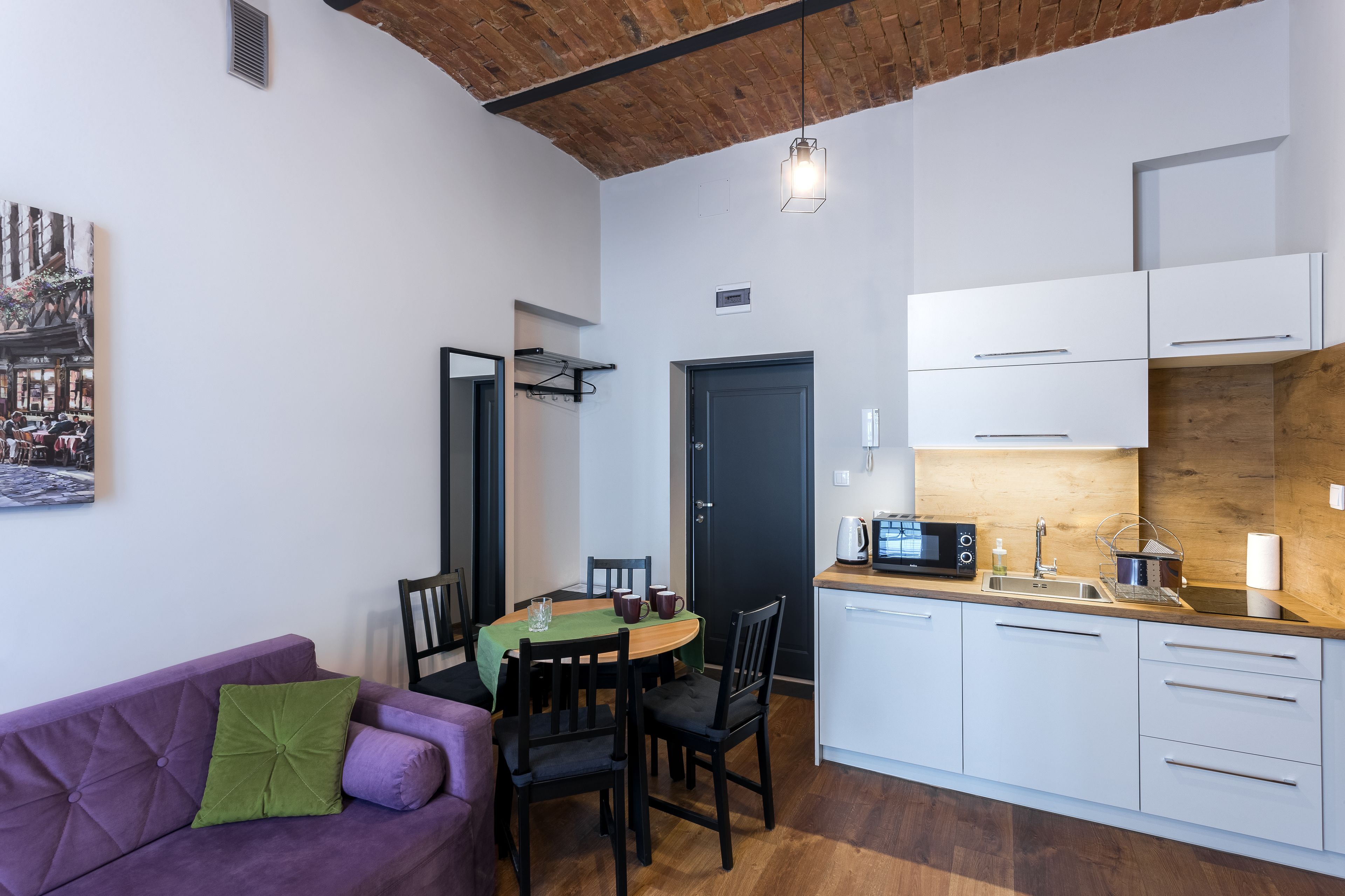 Una cucina funzionale con mobili bianchi, un tavolo da pranzo con sedie, un divano viola e un soffitto in legno.