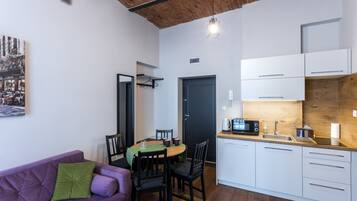 Una cucina funzionale con mobili bianchi, un tavolo da pranzo con sedie, un divano viola e un soffitto in legno.