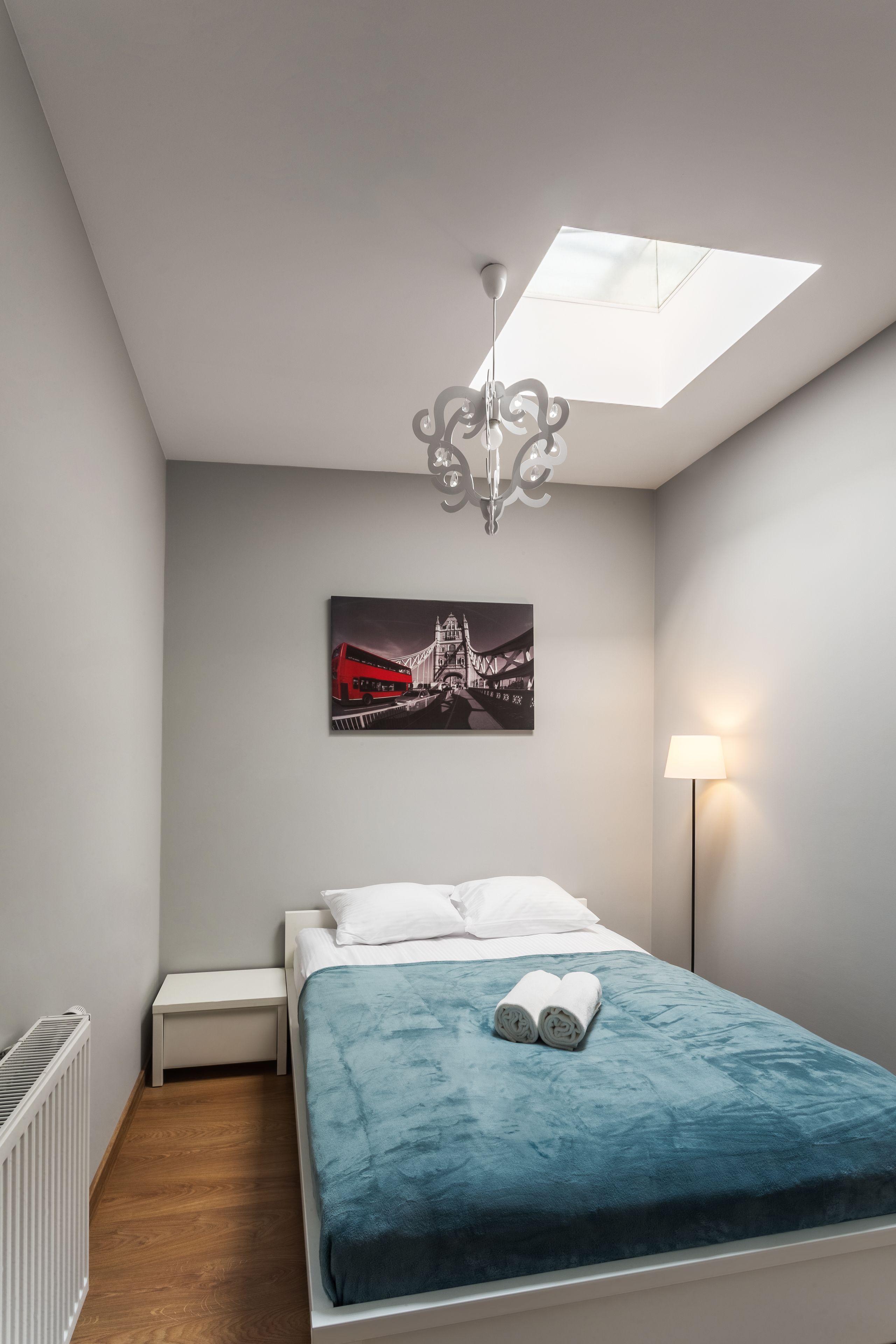 Ein Schlafzimmer mit einem Bett, einem Nachttisch, einem Heizkörper, einer Wandlampe und einer Deckenleuchte.