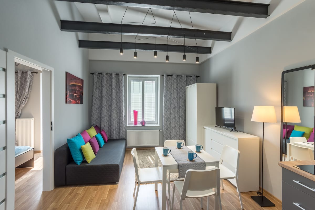 En moderne og kompakt opholdsstue med sofa, spisebord, stole, et fjernsyn og et spejl.