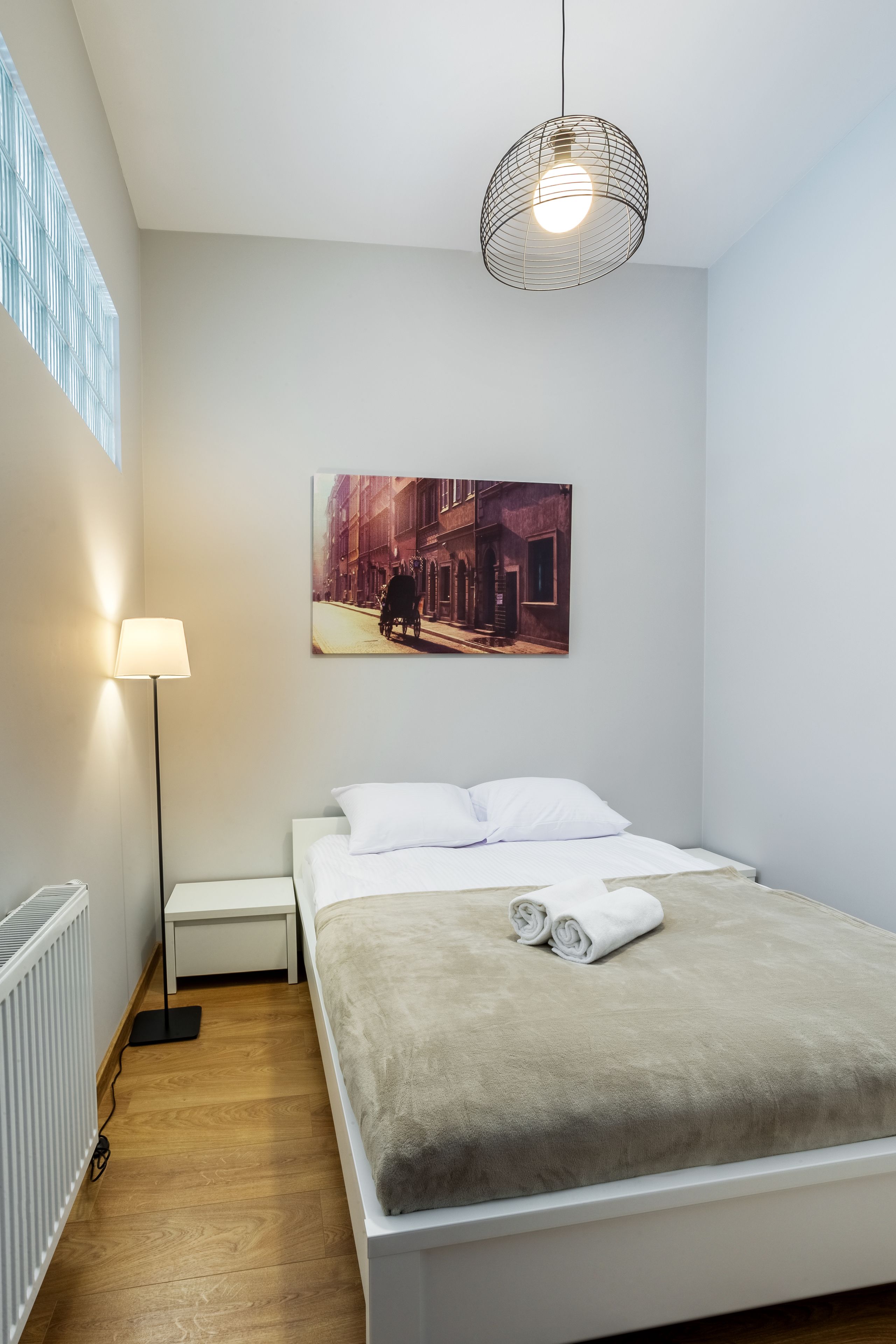 A neatly arranged bedroom with a bed, a bedside lamp, a floor lamp, and a wall-mounted picture.