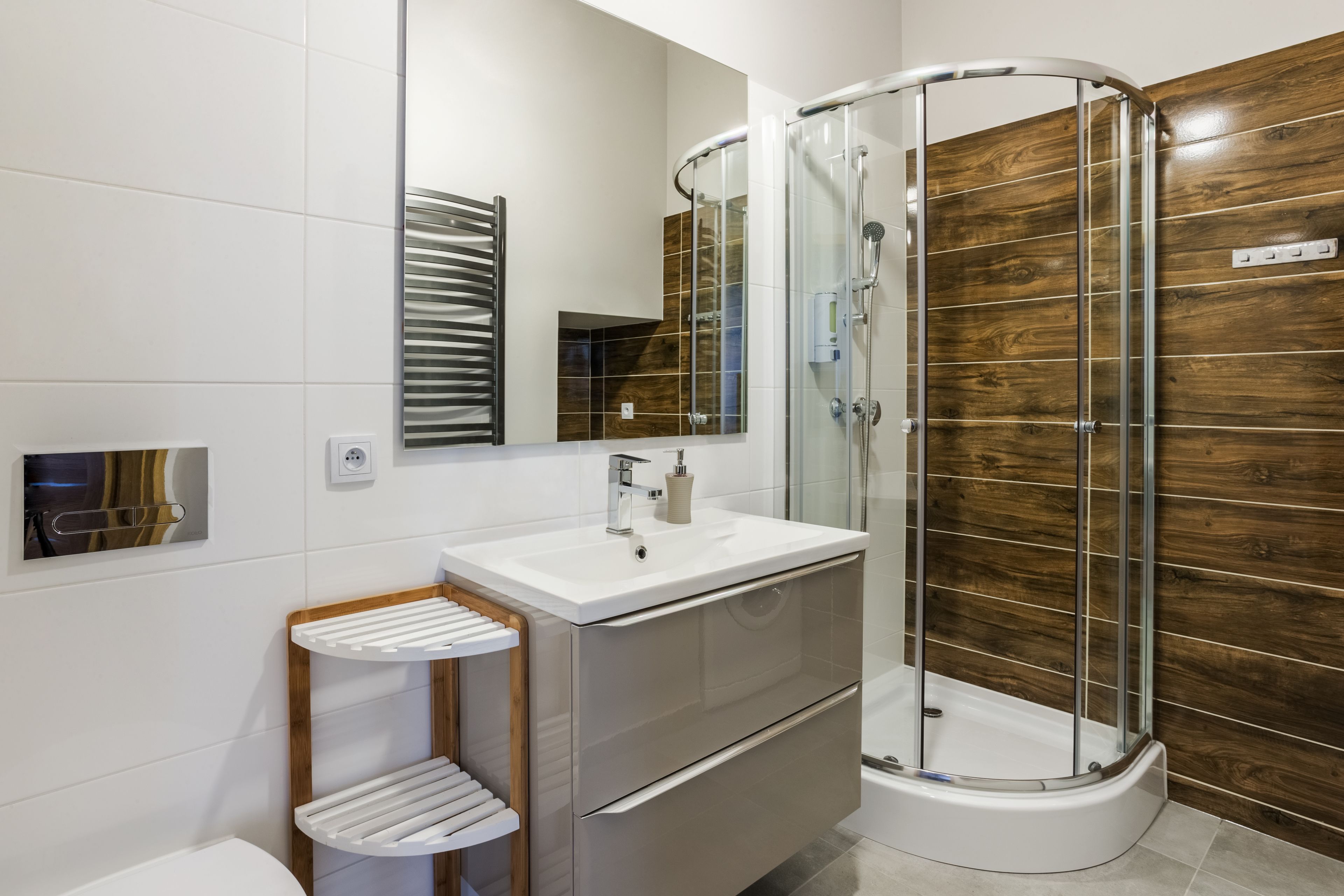 A modern bathroom with a glass-enclosed shower, a white sink, and a wooden vanity.