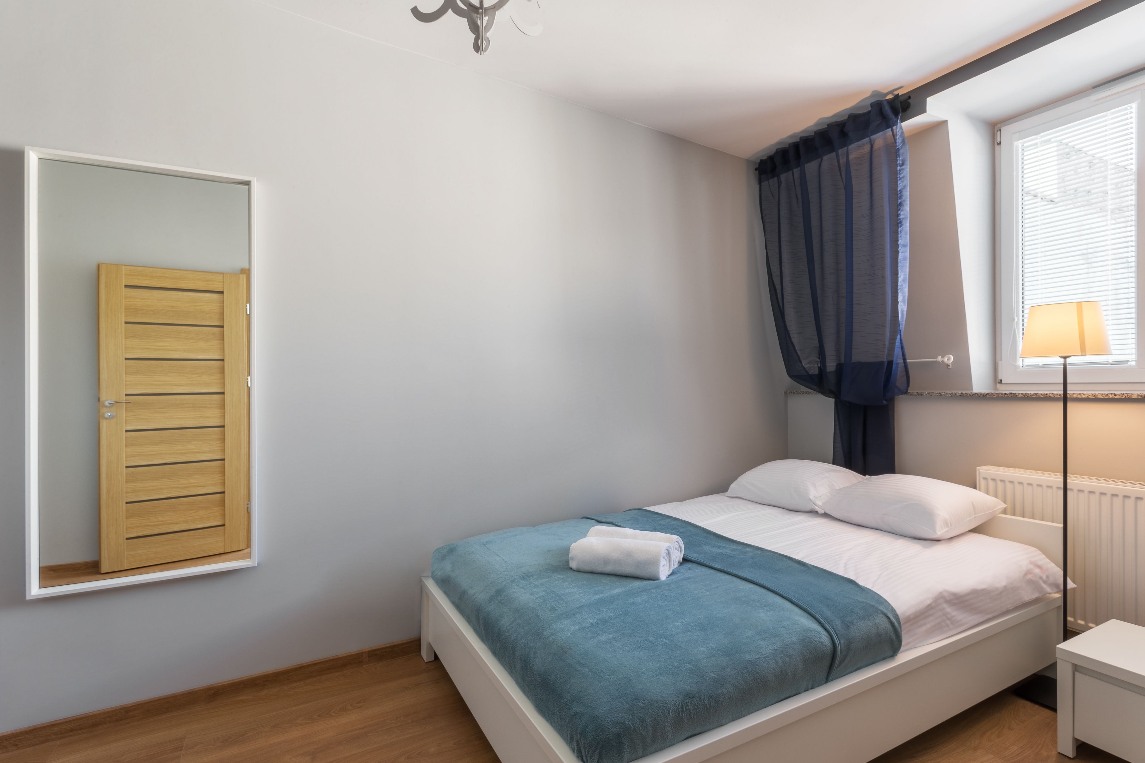 A bedroom with a bed, a window with blinds, a bedside lamp, and a wardrobe.