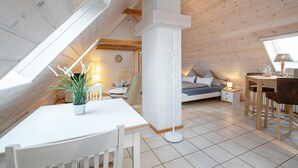 Un dormitorio acogedor en el ático, con techo inclinado, un comedor con mesa y sillas, y una mesita de noche con lámpara.