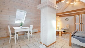 Una habitación acogedora con techo de madera, un escritorio blanco con silla, una cama y una mesita con lámpara.