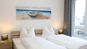 A neatly made bed with white bedding and pillows, a wooden headboard, and a painting of a boat on a beach above it.