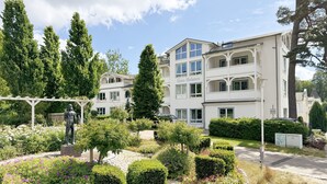A multi-story building named Haus Holstein with a garden featuring manicured hedges and flowers.