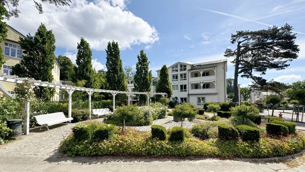 A courtyard with a white pergola, a bench, and well-maintained hedges.