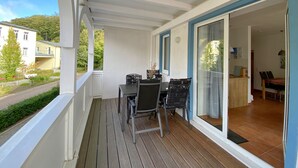 A balcony with a wooden floor, a table with chairs, and a view of a road and buildings.