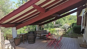Une terrasse extérieure dotée d’une plateforme en bois, d’un espace salon couvert avec un toit à rayures rouges et blanches, et d’un mur en pierre.