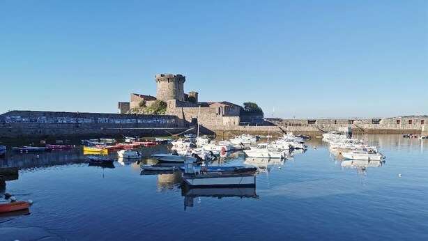 Un port où des bateaux sont amarrés près d’un ancien mur de pierre et d’une structure qui ressemble à un château.