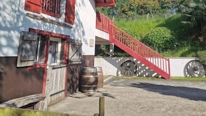 Un bâtiment avec un escalier rouge menant à un balcon, des barils à l’extérieur et un ciel bleu clair.