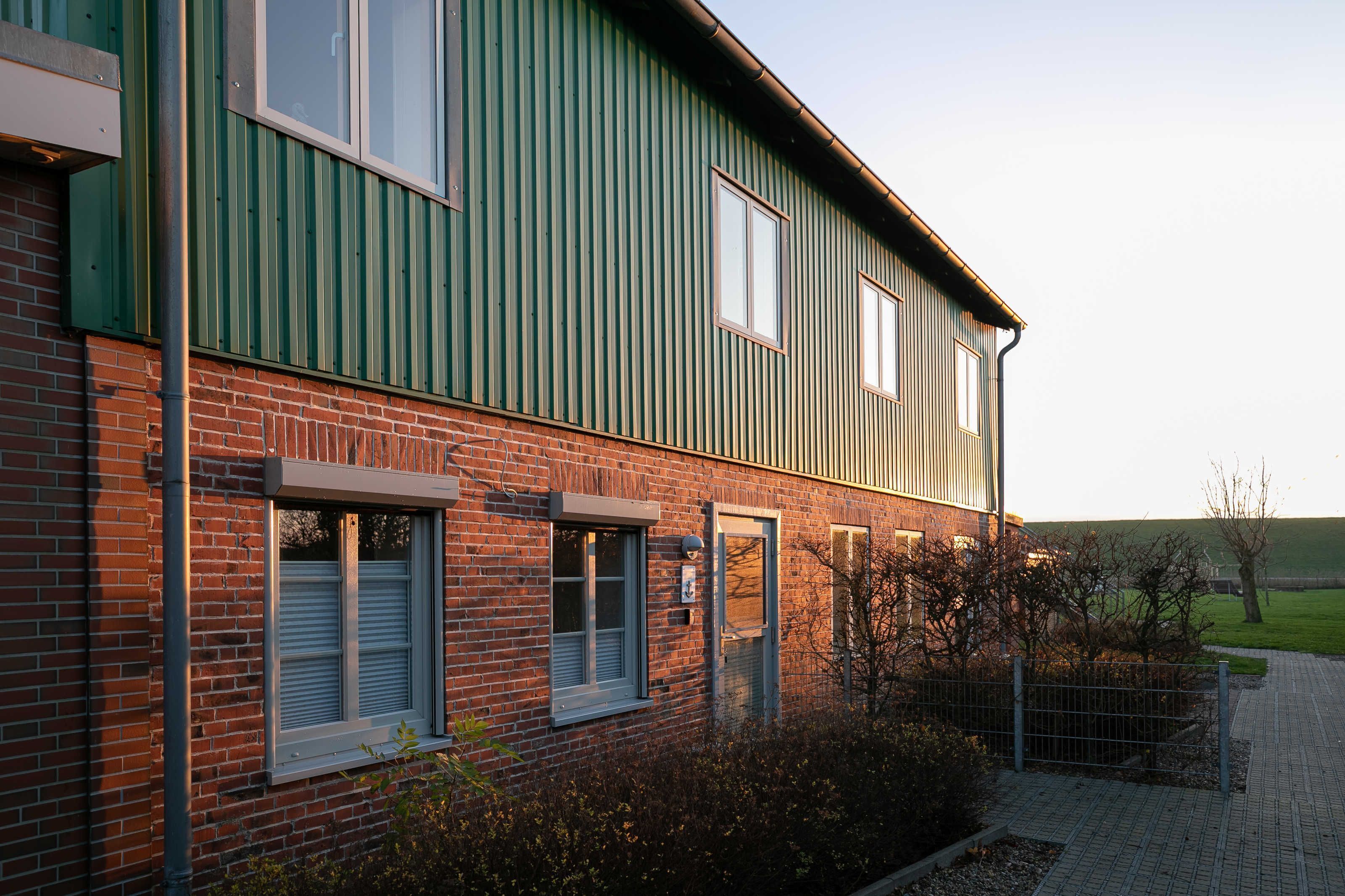 A two-story building with a green metal exterior and a brick base.