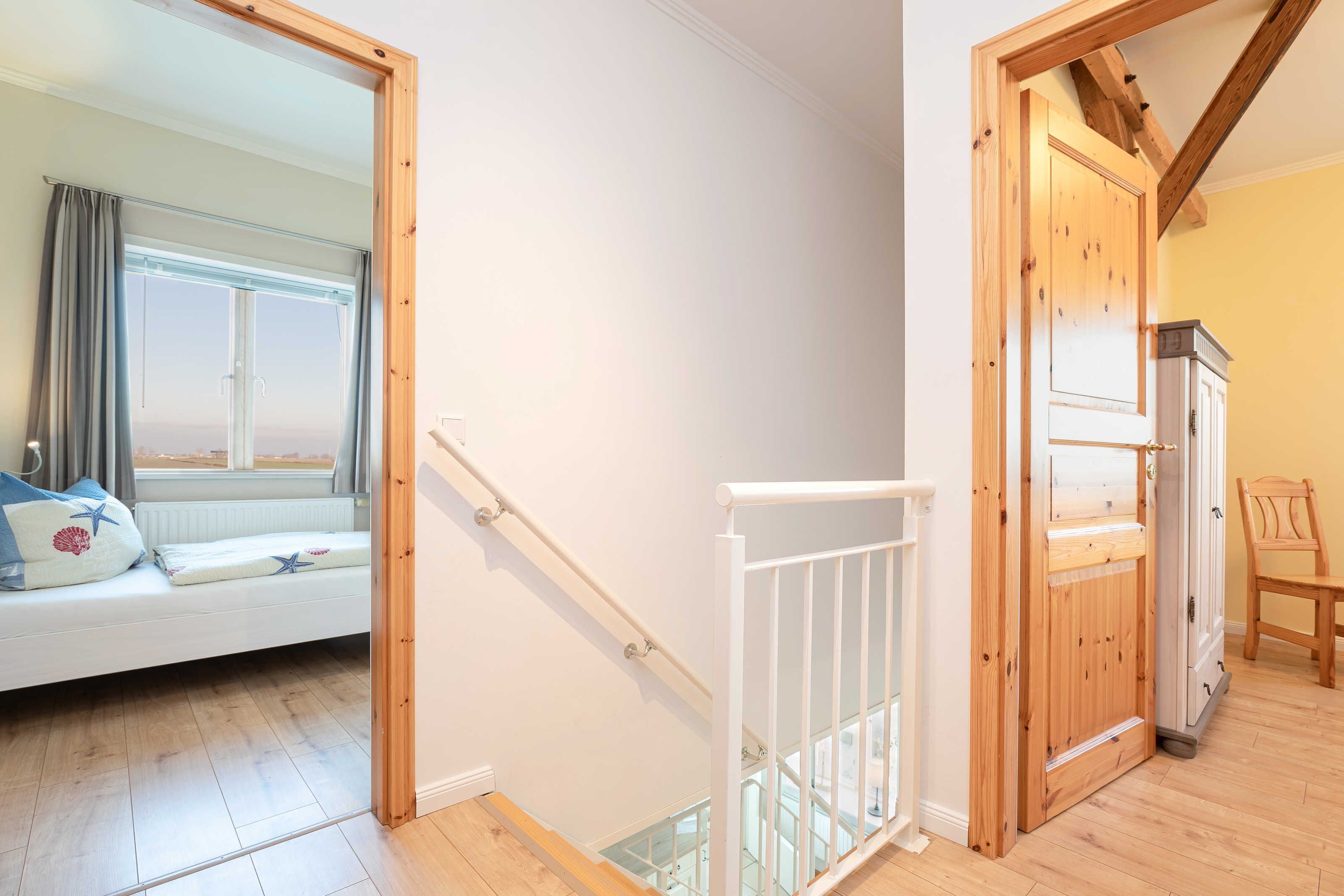 A staircase with a wooden railing leading to a room with a white sofa and a window with curtains.