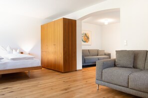 A bedroom with a bed, wooden wardrobe, grey sofa, and a painting on the wall.