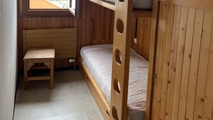 Une petite pièce en bois, avec des lits superposés, une petite table et une fenêtre donnant sur des immeubles.
